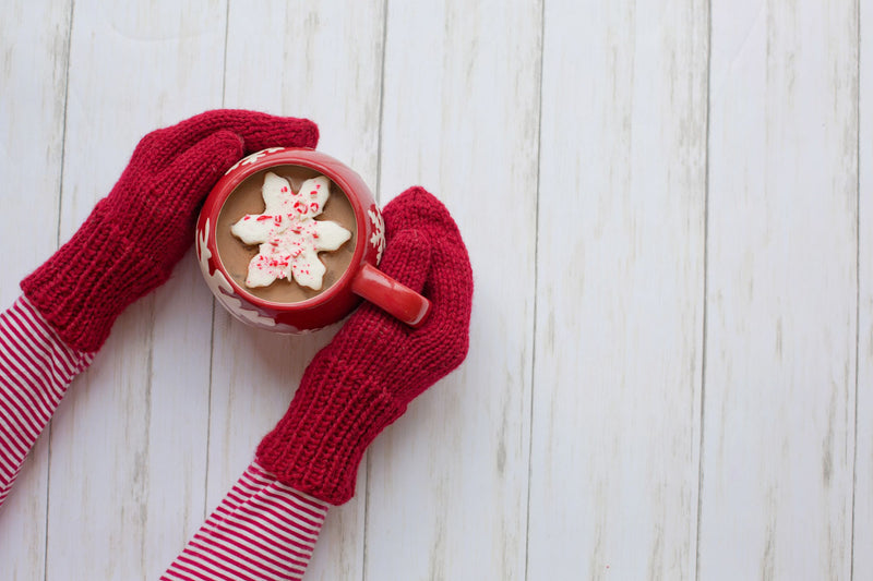 Knit mittens holding a mug of hot chocolate